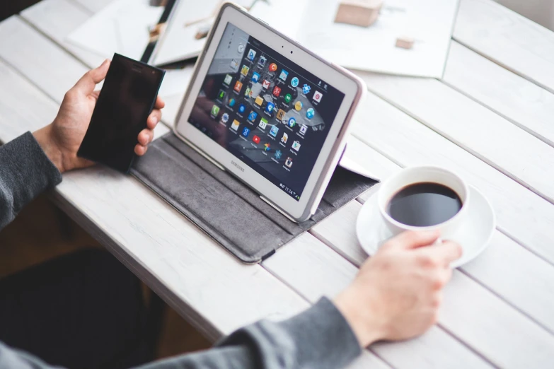 a person sitting at a table with a laptop and a cup of coffee, a picture, android phones, high quality]