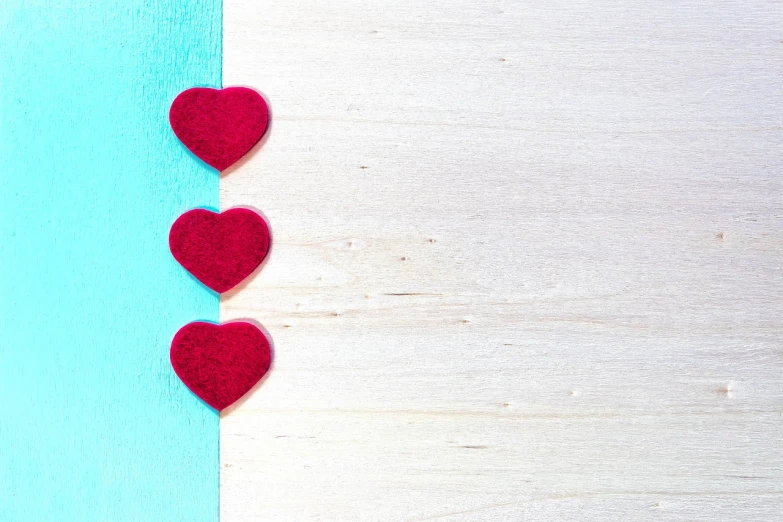 a couple of red hearts sitting on top of a blue and white wall, a stock photo, minimalism, made of wood, turquoise color scheme, three fourths view, layed on a red velvet fabric