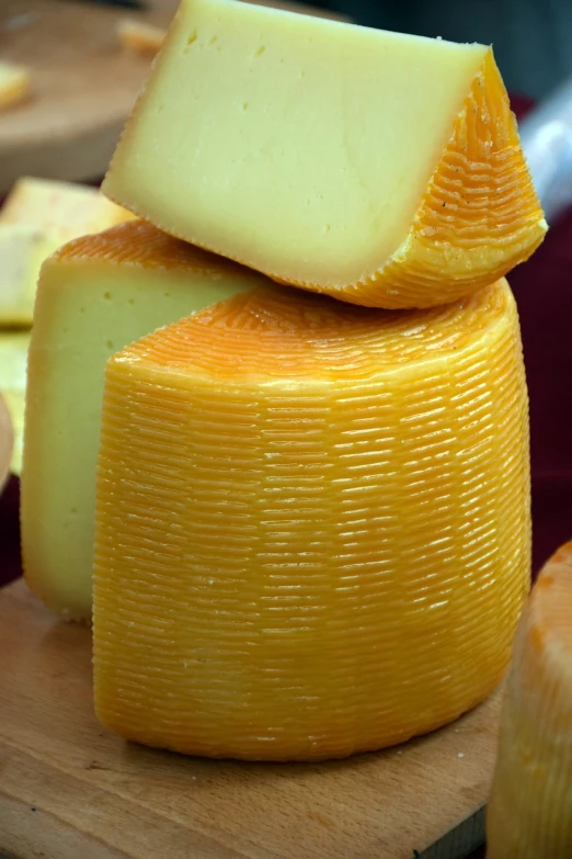 a pile of cheese sitting on top of a wooden cutting board, by Francisco de Holanda, renaissance, yellow aureole, very sharp detail, a pair of ribbed, shiny