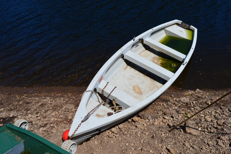 a white boat sitting on top of a beach next to a body of water, a photo, by Tom Carapic, pixabay, mini lake, hooked - up, injured, dingy