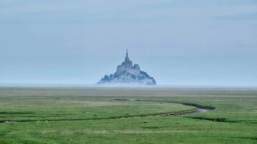 a large castle sitting on top of a lush green field, a picture, by Raphaël Collin, the rock is in the sea, hazy and misty, seen from the long distance, iconic composition