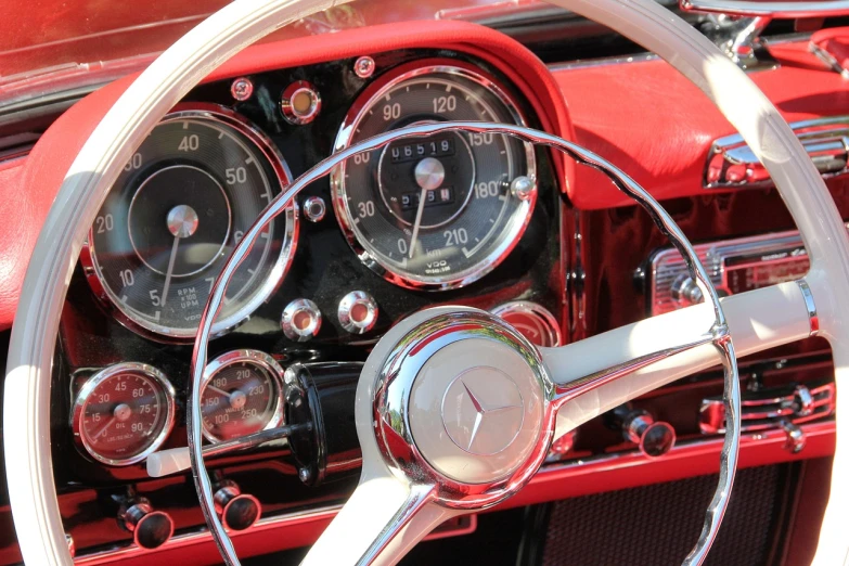 a close up of a steering wheel on a car, by Jim Nelson, pexels, retrofuturism, crimson and white color scheme, mercedez benz, tubes and gauges, 1961”