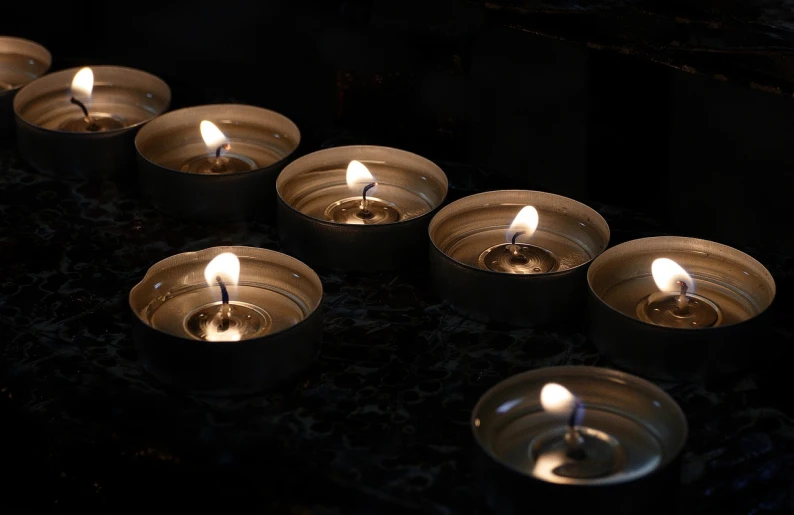 a row of lit candles sitting on top of a table, a picture, by Rhea Carmi, pexels, vanitas, praying, stock photo, glowing with silver light, high res photo