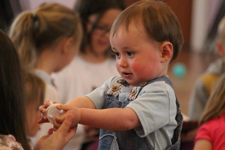 a close up of a child holding a nintendo wii controller, a picture, by Edward Corbett, process art, activity play centre, baptism, reaching out to each other, toddler