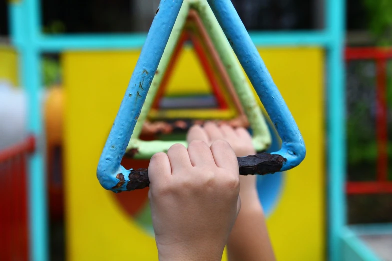 a close up of a child's hand holding a toy triangle, a picture, flickr, swings, hanging, artem chebokha, children playground