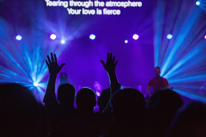a group of people that are standing in front of a stage, by Dave Allsop, happening, worship, with arms up, loving athmosphere, blue and purle lighting