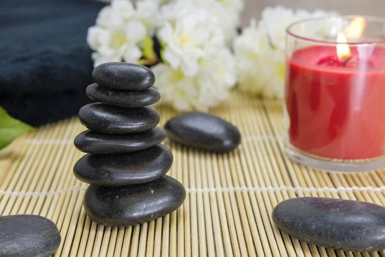 a stack of rocks sitting on top of a bamboo mat next to a candle, a still life, pixabay, red and black colors, stock photo, healthcare, full - length photo