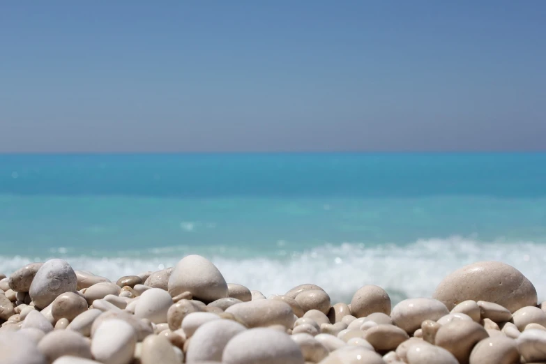 a pile of rocks sitting on top of a beach next to the ocean, a picture, by Alexis Grimou, blue! and white colors, mediterranean beach background, jasmine, sap