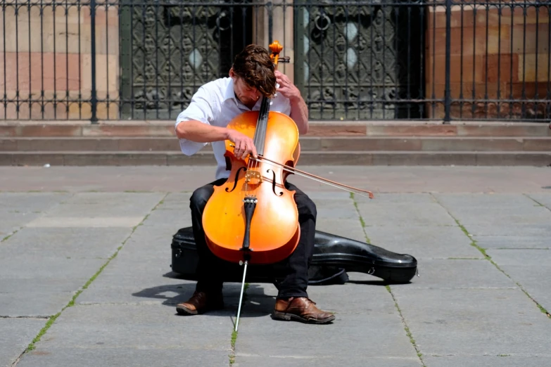 a man sitting on the ground playing a cello, by Erwin Bowien, flickr, glasgow, in a square, a super-smart, amber