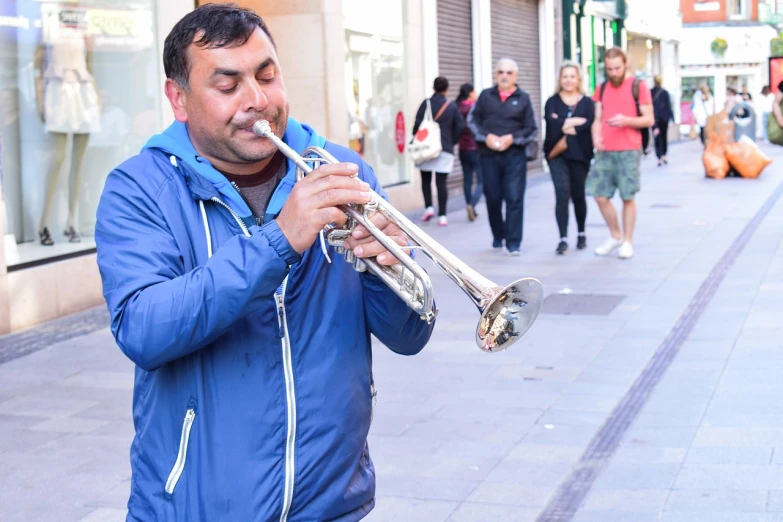 a man in a blue jacket playing a trumpet, a photo, long street, with a happy expression, costa blanca, shiny brass