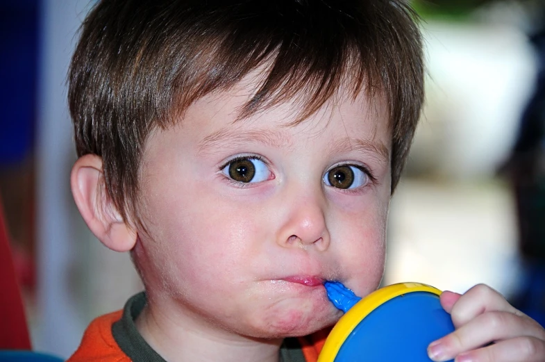 a close up of a child with a toy in his mouth, a picture, holding a drink, noticeable tear on the cheek, short brown hair and large eyes, the straw is in his mouth