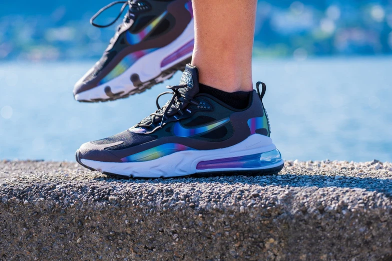 a person standing on a ledge next to a body of water, shutterstock, holography, nike air max, colourful close up shot, avatar image, f 2 0