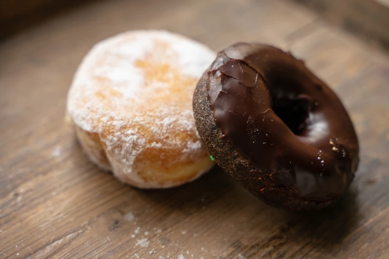 a couple of doughnuts sitting on top of a wooden table, by Dietmar Damerau, hurufiyya, chocolate, upclose, 🦩🪐🐞👩🏻🦳, close up angle