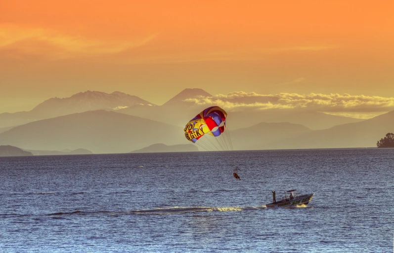 a person parasailing in the ocean with mountains in the background, a picture, by Matt Stewart, shutterstock, colours of the sunset, seattle, tonemapped, caulfield