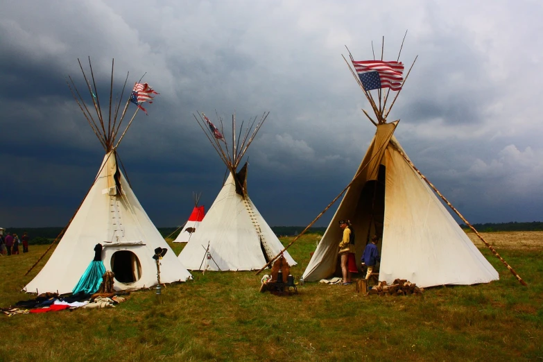 a group of teepees sitting on top of a grass covered field, by Robert Lee Eskridge, flickr, sots art, standing against the storm, american flags, movie set”, 8k))