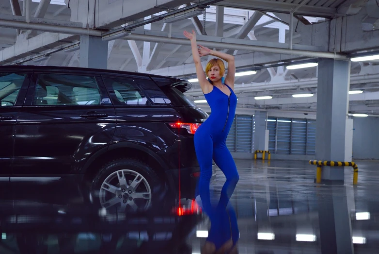 a woman in a blue jumpsuit standing next to a black car, a hologram, inspired by David LaChapelle, trending on cg society, she is dancing. realistic, nicki minaj curvy, indoor shot, blonde goddess