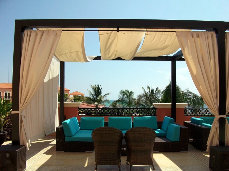 a gazebo sitting on top of a patio covered in blue cushions, background made of big curtains, aruba, rooftop, cream - colored room