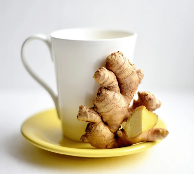 a white cup sitting on top of a yellow plate, inspired by Wlodzimierz Tetmajer, shutterstock, ginger, set against a white background, hr ginger, herbs