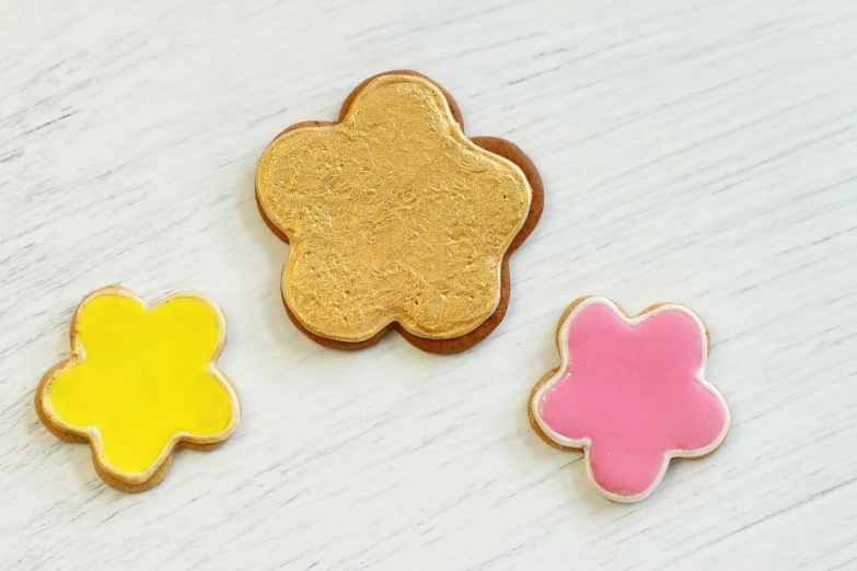 a couple of cookies sitting on top of a table, a picture, flower power, contour, golden shapes, miniature product photo