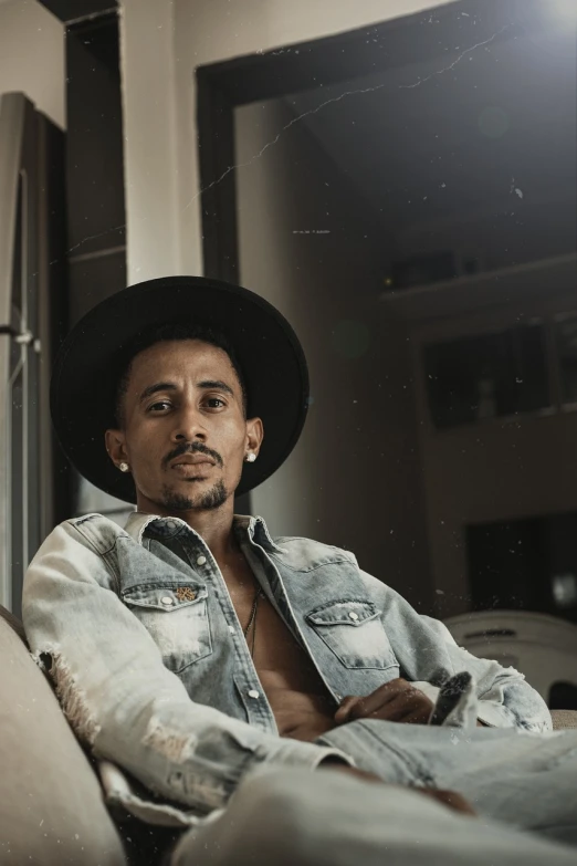 a man sitting on a couch wearing a hat, a portrait, inspired by Afewerk Tekle, pexels, thiago alcantara, ashteroth, attractive pose, portrait of tall