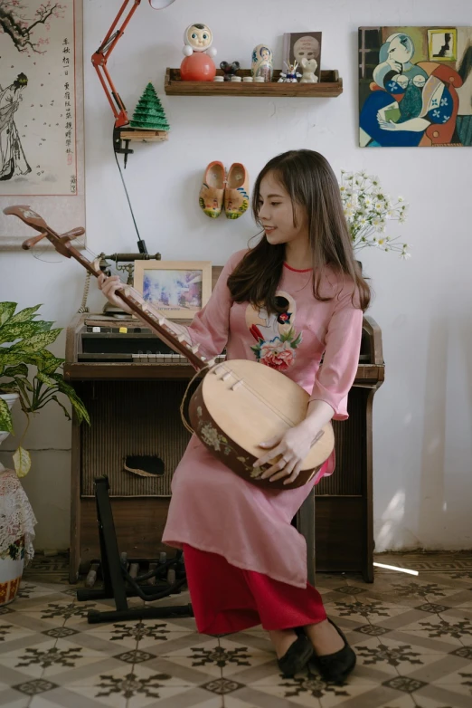 a woman sitting on a chair playing a banjo, inspired by Gu Kaizhi, ao dai, at home, cutecore, wearing pink floral chiton