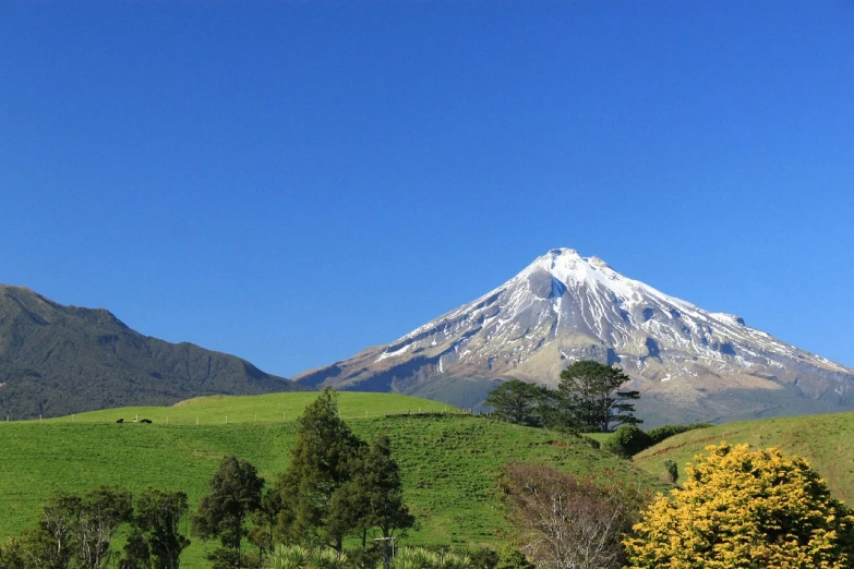 a large mountain towering over a lush green hillside, by Gawen Hamilton, flickr, hurufiyya, mount doom, beautiful sunny day, snow capped mountains, from lord of the rings