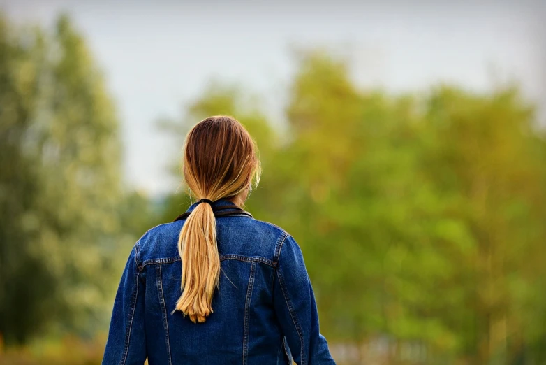 a woman in a denim jacket holding a frisbee, by Niko Henrichon, shutterstock, walking away, header, trees in the background, student