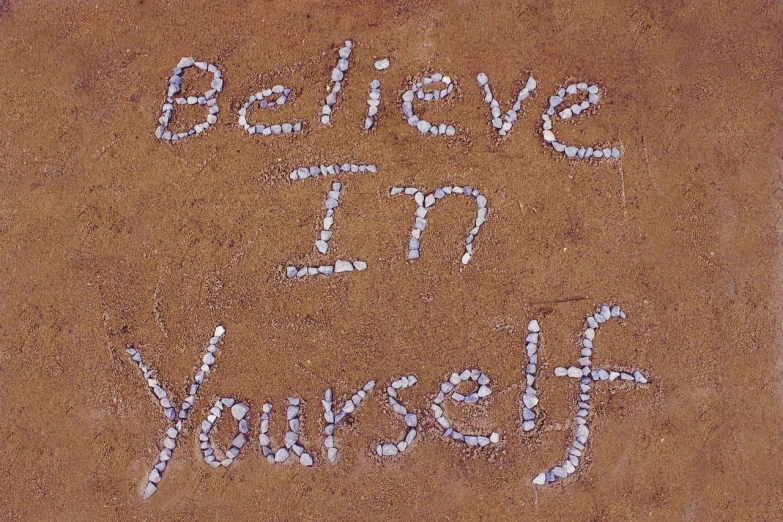 the words believe in yourself written on the ground, inspired by Henri Bellechose, full of sand and glitter, narcissist, we can do it, collective consciousness