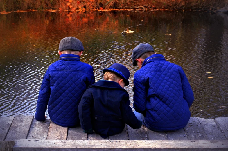 a group of people sitting on a dock next to a body of water, a picture, by Jan Rustem, pexels, cute boys, blue jacket, berets, sitting at a pond