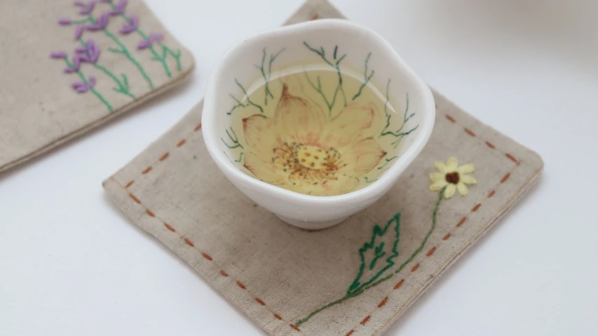 a close up of a cup of tea on a table, a detailed painting, by Maki Haku, flickr, pressed flowers, fabric embroidery, colored milk tea, with yellow cloths