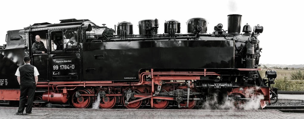 a man standing next to a black and red train, a portrait, by Thomas Häfner, trending on pixabay, brass and steam technology, panoramic, drooling ferrofluid. dslr, looking from side and bottom!