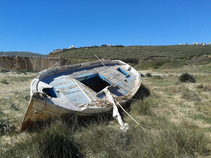 a boat sitting on top of a grass covered field, by Altichiero, flickr, les nabis, washed up, greek setting, front side full, ios