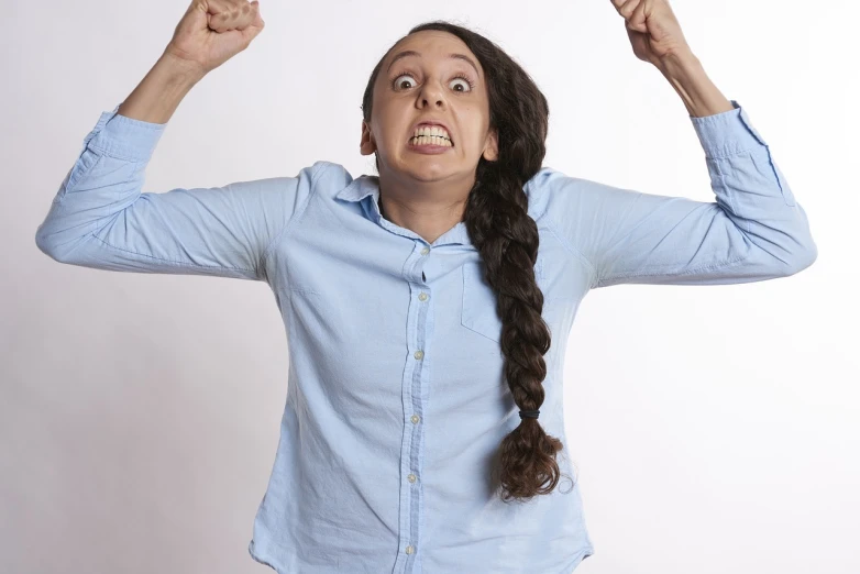 a woman in a blue shirt has her arms in the air, a picture, by Juan O'Gorman, pexels, antipodeans, angry face, oona chaplin, rebecca sugar, hunched shoulders