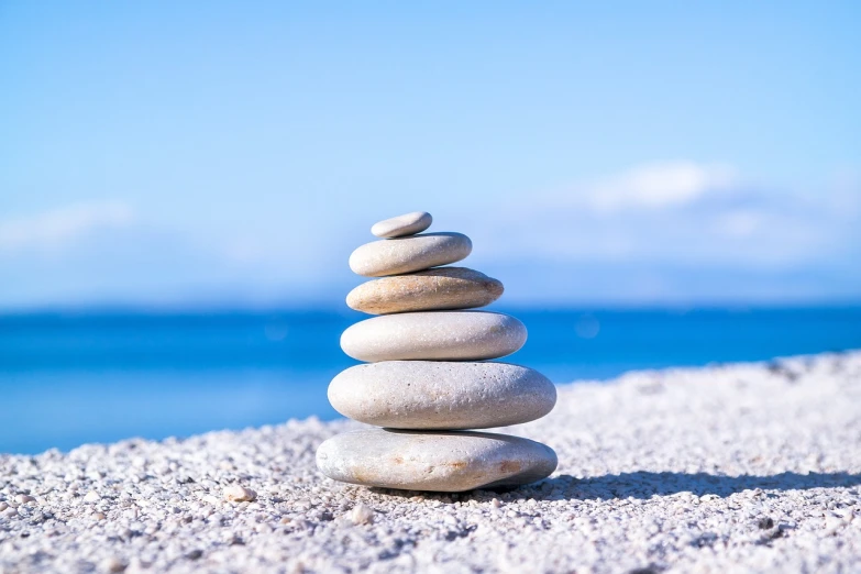 a stack of rocks sitting on top of a sandy beach, minimalism, tai chi, relaxed. blue background, short in stature, white stones