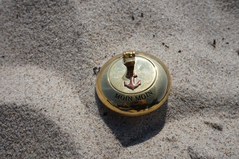a golden bell sitting on top of a sandy beach, by Romain brook, metal lid, mochiduki key, nautical siren, gold plated