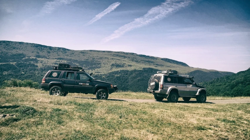 two vehicles parked on the side of a dirt road, a picture, unsplash, figuration libre, the alps are in the background, banner, fuji 8 0 0 film, arrendajo in avila pinewood