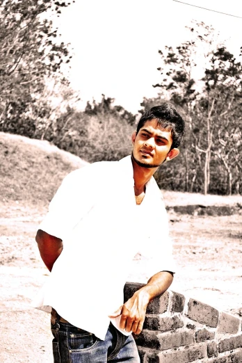 a man standing next to a brick wall, a picture, inspired by Bikash Bhattacharjee, hurufiyya, white monochrome color!!!!!, amidst nature, around 20 yo, colors white!!