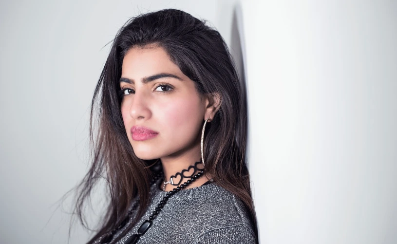 a beautiful young woman leaning against a wall, a picture, inspired by Maryam Hashemi, pexels, hurufiyya, mia khalifa, acting headshot, black jewellery, silver earring