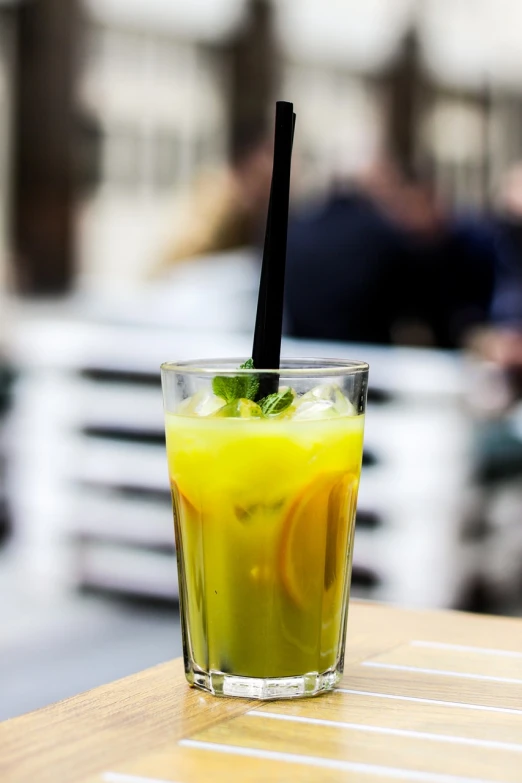 a drink sitting on top of a wooden table, by Mathias Kollros, pexels, hurufiyya, yellow and greens, in a sidewalk cafe, yellow-orange, mixing drinks