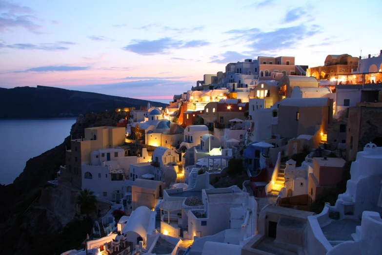 a group of buildings sitting on top of a hill next to a body of water, a picture, happening, beautiful and spectacular dusk, greek nose, gaudy, whitewashed buildings