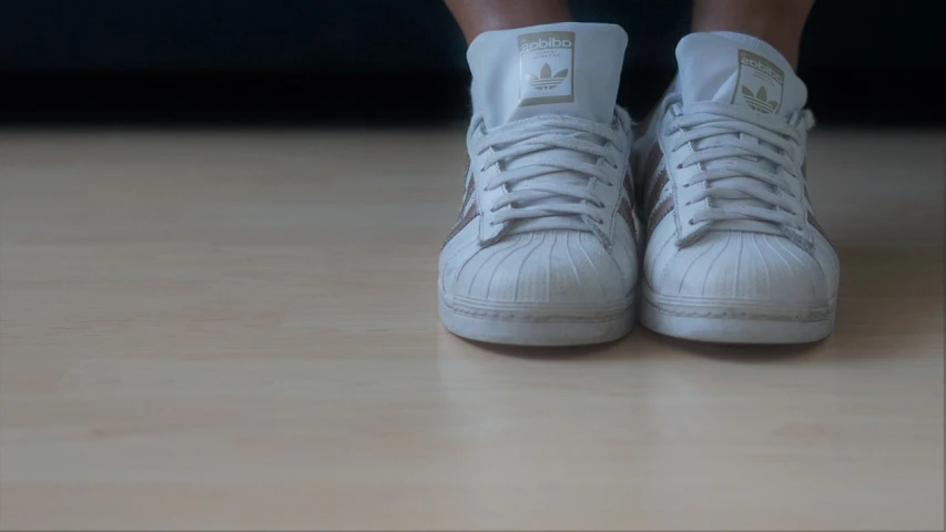 a pair of white sneakers sitting on top of a wooden floor, by Christen Købke, hyperrealistic flickr:5, wearing adidas clothing, low quality footage, wearing a brown