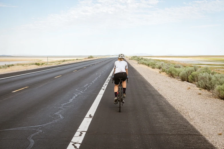 a man riding a bike down the middle of a road, a picture, by Whitney Sherman, shutterstock, on a desolate plain, long shot from back, picture of a female biker, usa-sep 20