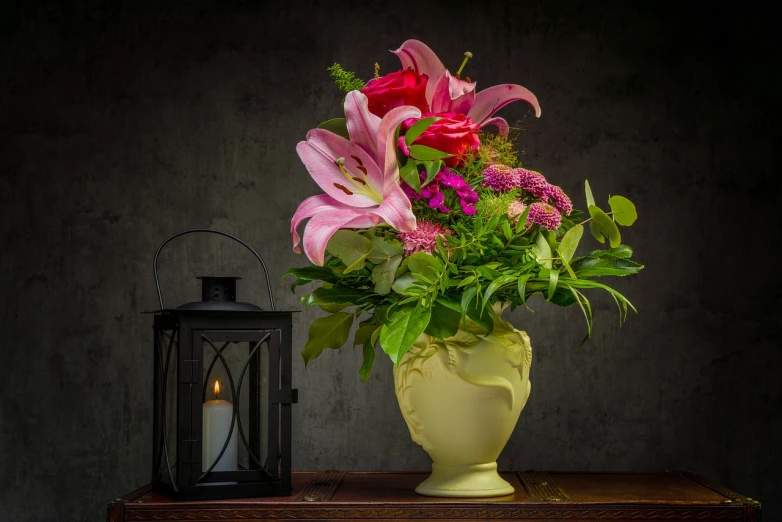 a vase filled with lots of flowers next to a lantern, a still life, inspired by Martin Johnson Heade, shutterstock, good lighted photo, lilies, draped in fleshy green and pink, very accurate photo