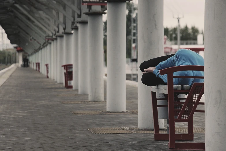 a person sitting on a bench at a train station, pexels, realism, movie still of a tired, blueish, benches, cinestill 800t 50mm