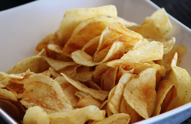 a white bowl filled with potato chips on top of a table, inspired by Chippy, pexels, process art, 3/4 view from below, computer chips, wikimedia, bottom body close up