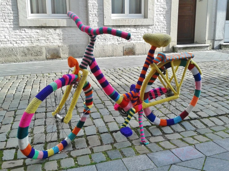 a knitted bicycle is parked on a cobblestone street, a surrealist sculpture, flickr, full of colour w 1024, belgium, whoa, twirly