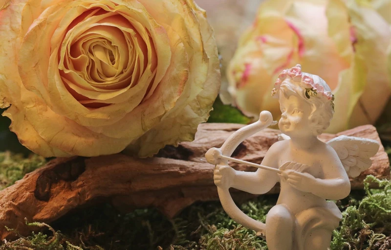 a close up of a figurine of a cupid with a rose in the background, a picture, by Marie Angel, romanticism, beautiful composition 3 - d 4 k, flower decorations, rustic setting, yellow rose