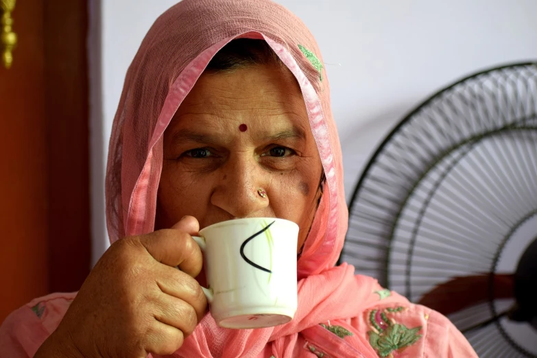 a woman drinking a cup of coffee in front of a fan, a portrait, by Rajesh Soni, flickr, pink face, older woman, patriotism, mugshot