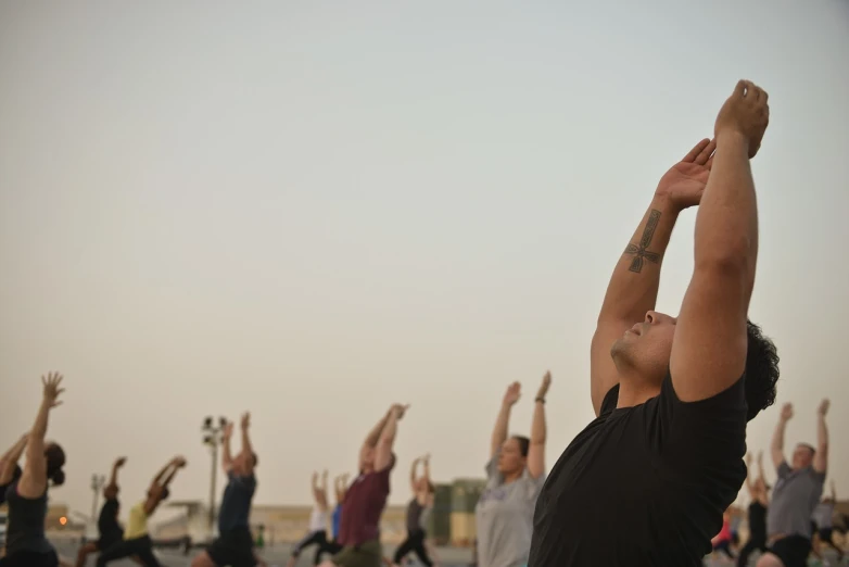 a group of people doing yoga on a beach, a photo, pexels, renaissance, man standing in defensive pose, skies behind, dubai, lit from the side