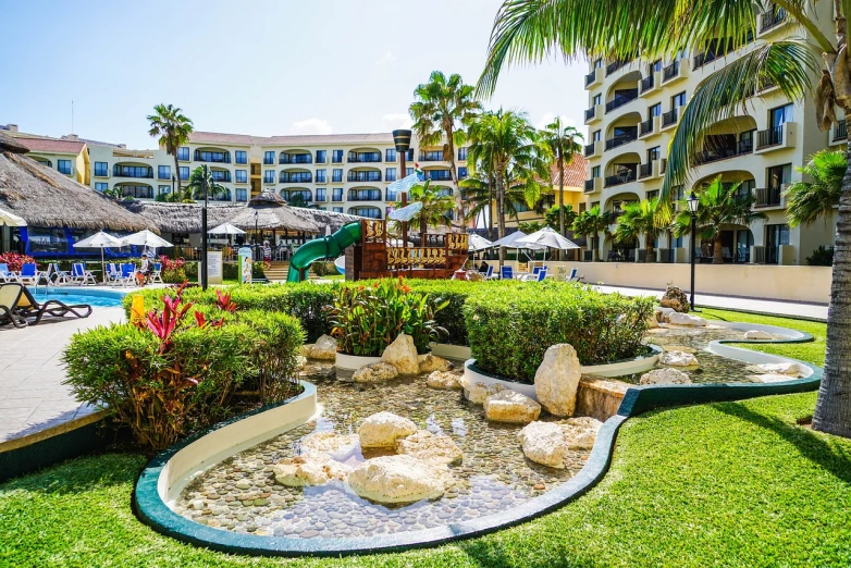 an outdoor swimming pool surrounded by palm trees, flowerbeds, aruba, playground, lowres